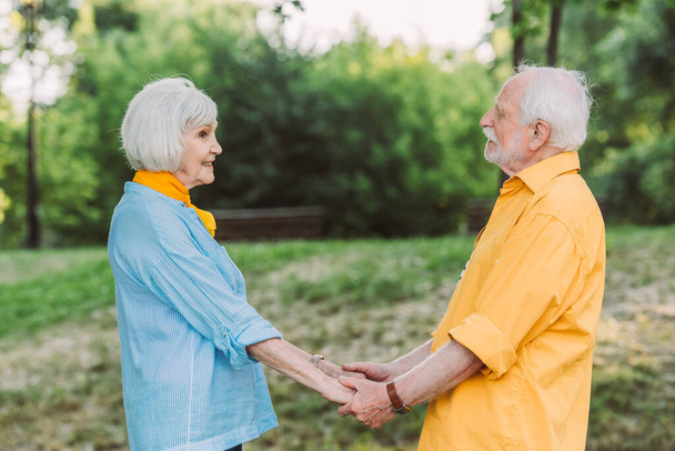 Side view of senior woman smiling while holding hands of husband in park  - Photo, Image