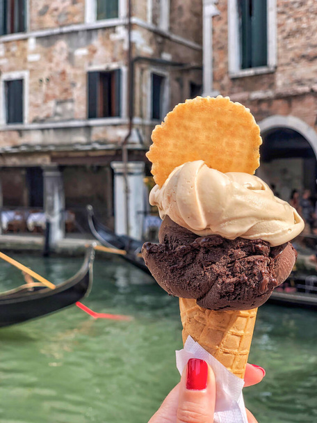 une main tenant de la crème glacée sur un cône de gaufre contre des gondoles dans le canal de Venise en Italie - Photo, image