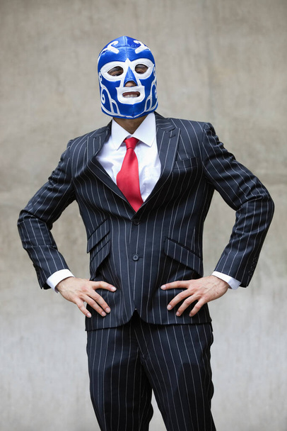 Young businessman in pinstripes suit and wrestling mask over gray background - Photo, Image