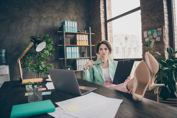 Photo of attractive attentive minded business boss lady notebook table distance home work hold documents contract clipboard look screen legs on table chief sit chair modern office indoors - Фото, зображення
