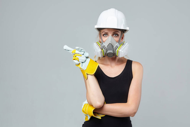 blonde girl. in a respirator and protective helmet and gloves indicates an empty space. construction concept - Фото, изображение