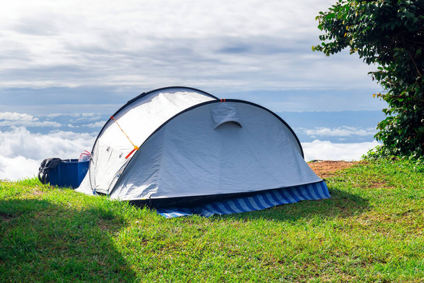 Feche uma tenda de acampamento que está montada em um campo de grama no ponto mais alto de uma montanha alta com um pano de fundo de céu e nuvens
. - Foto, Imagem