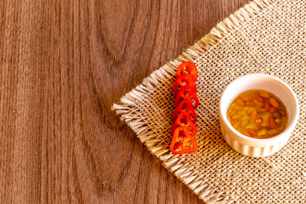 Small bowl with oil and pepper on rustic wooden background. - Photo, Image