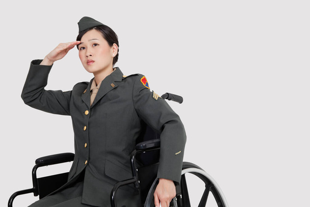 Female US military officer in wheelchair saluting over gray backgrounds - Photo, Image