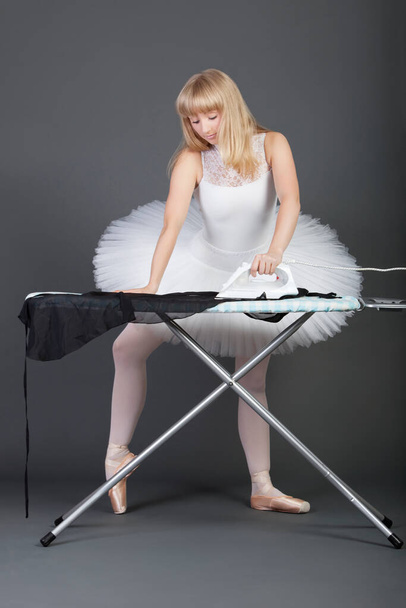 Young female ballet dancer ironing over grey background - Foto, imagen