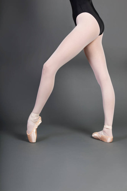Low section of young ballet dancer wearing ballet slippers over grey background - Fotoğraf, Görsel