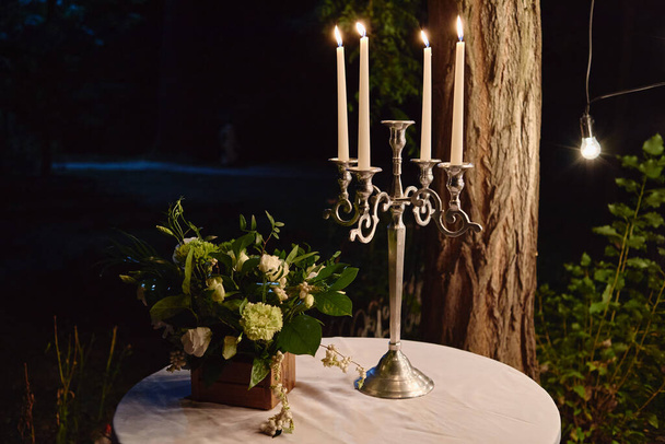 Night wedding decoration with candles and flowers on table, bulb lights on tree outdoors, copy space - Photo, Image