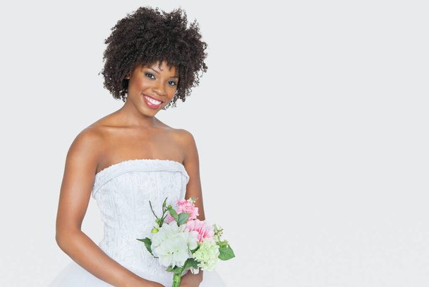 Portrait of beautiful African American bride holding bouquet over gray background - Fotoğraf, Görsel