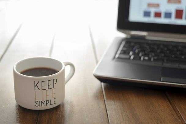 tasse à café avec message garder la vie simple sur une table en bois et un ordinateur hors foyer en arrière-plan - Photo, image