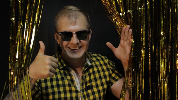 Portrait of caucasian man posing on black background. Gold shining foil strips. Party, music, disco - Photo, Image