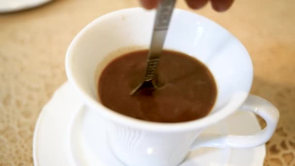 Close-up of person hand stirring coffee with spoon in a white cup on wooden table background. - Filmati, video