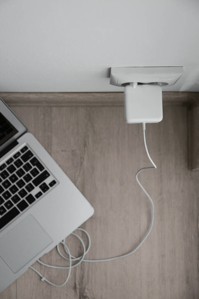 Modern laptop charging from electric socket, top view - Foto, Imagen