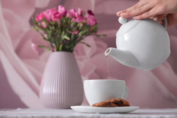 Woman pouring hot tea into cup at table, closeup - Fotoğraf, Görsel