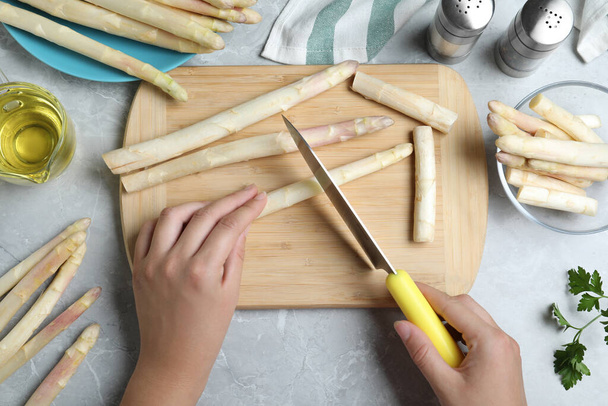 Woman cutting fresh white asparagus at grey marble table, top view - Foto, Imagem
