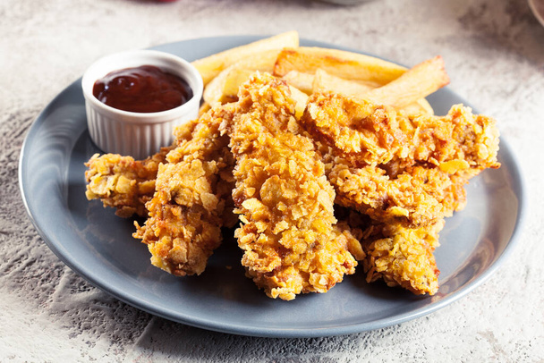 Chicken strips in cornflakes breadcrumb served with french fries - Fotó, kép