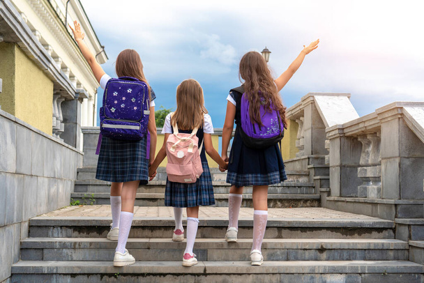 Uczniowie w szkolnych mundurkach idą schodami do szkoły przeciwko błękitnemu niebu. Ręce do góry. Widok z tyłu. - Zdjęcie, obraz