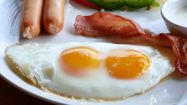 Osoba jedząca śniadanie. Śniadanie w stylu amerykańskim ze smażonymi jajkami, bekonem z grilla, kiełbasą i sałatką warzywną. Koncepcja zdrowej żywności. - Materiał filmowy, wideo