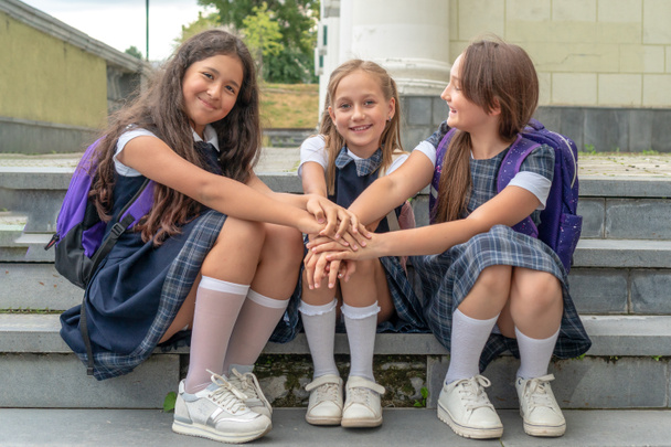 Μαθητές με σχολική στολή κάθονται στις σκάλες και κρατιούνται χέρι χέρι. Η έννοια της σχολικής φιλίας και των ευτυχισμένων παιδιών. - Φωτογραφία, εικόνα