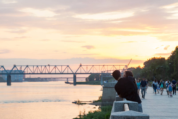 Novosibirsk, Russia - 07.12.2020: Una coppia amorevole si abbraccia mentre cammina lungo l'argine al tramonto nell'ora d'oro in estate vicino al fiume. - Foto, immagini
