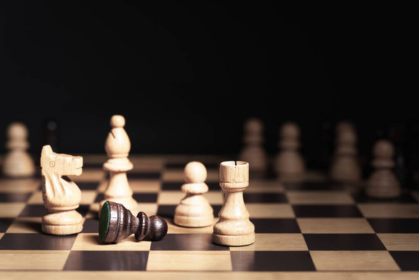 Zbliżenie, Czarny pionek leży na szachownicy i otoczony jest przez białego rycerza, gońca, wieżę i pionka. Inne szachy w tle. Władza, Black Lives Matter i koncepcja praw człowieka - Zdjęcie, obraz
