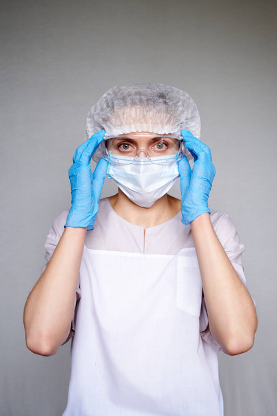 Primo piano di medico o scienziato donna con maschera medica, cappuccio chirurgico, occhiali e mani in guanti su sfondo grigio. - Foto, immagini