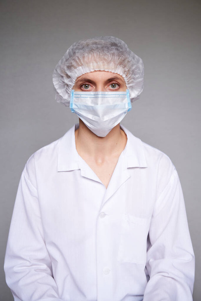 Крупный план женщины-врача или ученого с медицинской маской и хирургической шапкой на сером фоне. - Фото, изображение