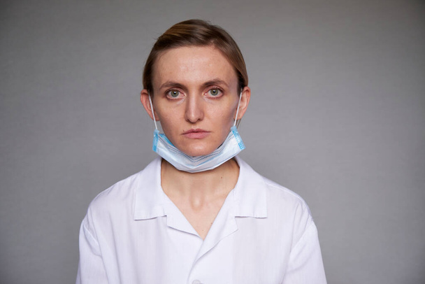 Gros plan d'une femme médecin ou scientifique portant un masque facial protecteur sur fond gris. Masque médical est abaissé au menton - Photo, image
