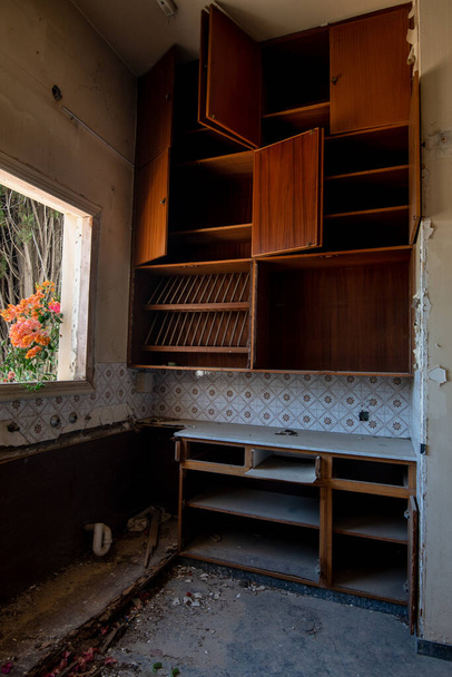 Zarar görmüş ahşap mobilyalar ve penceresinde çiçek olan terk edilmiş eski bir ev mutfağının içinde. - Fotoğraf, Görsel