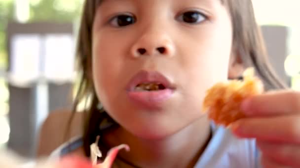 Onnellinen lapsi tyttö nauttia syömällä paistettua kanaa ja ranskalaisia perunoita palvelukaupassa. Roskaruoka ja terveyskäsitteet. - Materiaali, video