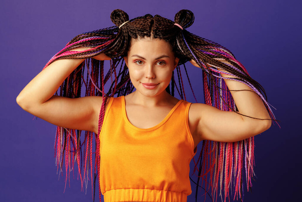 Smiling positive young woman with colorful african braids on purple background - Φωτογραφία, εικόνα