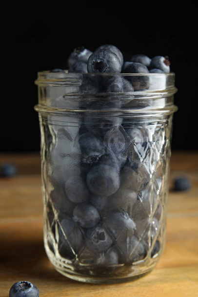 Tasty ripe blueberries in glass jar on wooden table - Photo, image