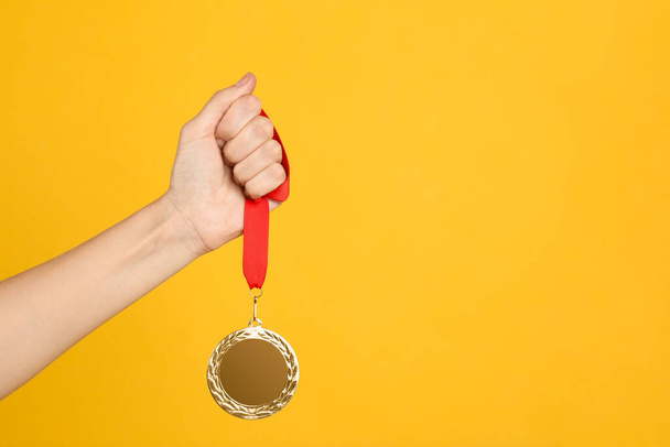 Woman holding golden medal on yellow background, closeup. Space for design - Foto, afbeelding