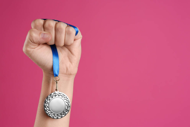 Woman holding silver medal on pink background, closeup. Space for design - Foto, afbeelding