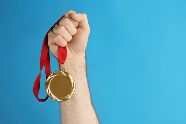Man holding golden medal on blue background, closeup. Space for design - Zdjęcie, obraz