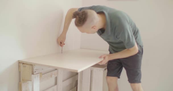 Jovem loira caucasiano com um homem Bun está parafusando manualmente uma mesa construída com paletes de madeira
  - Filmagem, Vídeo