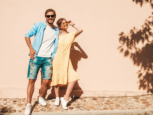 Portrait of smiling beautiful girl and her handsome boyfriend. Woman in casual summer dress and man in jeans. Happy cheerful family. Female having fun in the street near wall - Foto, immagini
