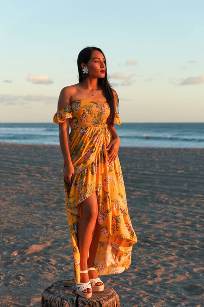 Um elegante modelo feminino branco jovem posando na praia em um belo vestido amarelo com padrões florais
 - Foto, Imagem