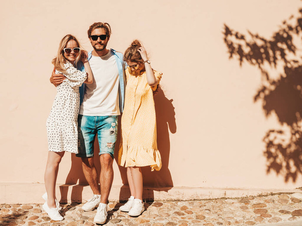 Group of young three stylish friends posing in the street. Fashion man and two cute girls dressed in casual summer clothes. Smiling models having fun in sunglasses.Cheerful women and guy going crazy - Foto, afbeelding