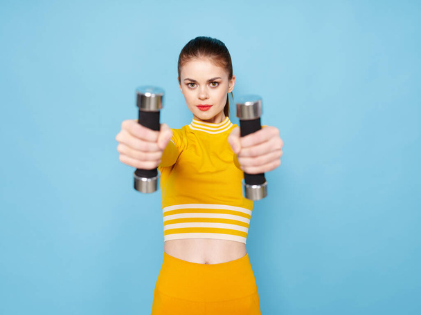 Woman in a yellow sweater with dumbbells in her hands and a bright makeup  - Foto, imagen