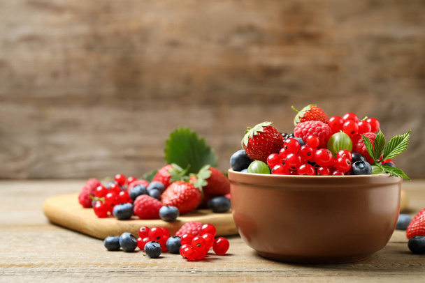 Mix of different fresh berries in bowl on wooden table. Space for text - Foto, afbeelding