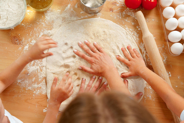 Mother and her kids kneading dough on kitchen table - Foto, afbeelding