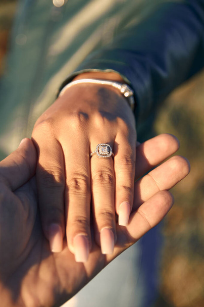 Közelkép egy párról, akik fogják egymás kezét és megmutatják a gyűrűt. - Fotó, kép