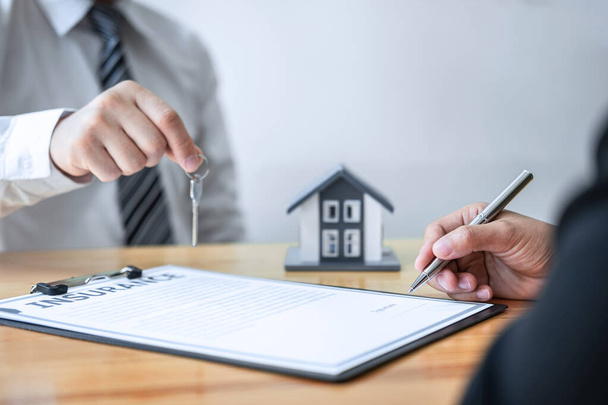 Kotivakuutus ja kiinteistösijoitusten käsite, Myyntiedustaja, joka antaa talon avaimen uudelle asiakkaalle allekirjoitettuaan sopimuksen hyväksytyn kiinteistöhakemuksen kanssa
. - Valokuva, kuva
