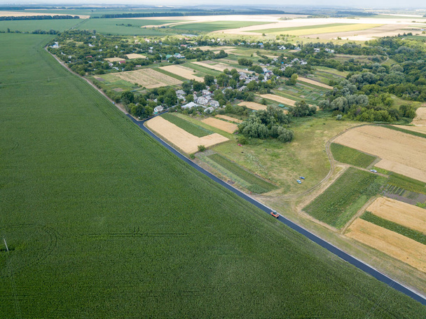 ウクライナの緑のトウモロコシ畑近くのアスファルト道路。空中ドローンビュー. - 写真・画像