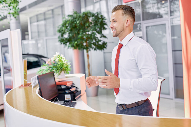 pleasant salesman welcomes customers in dealership - Фото, изображение