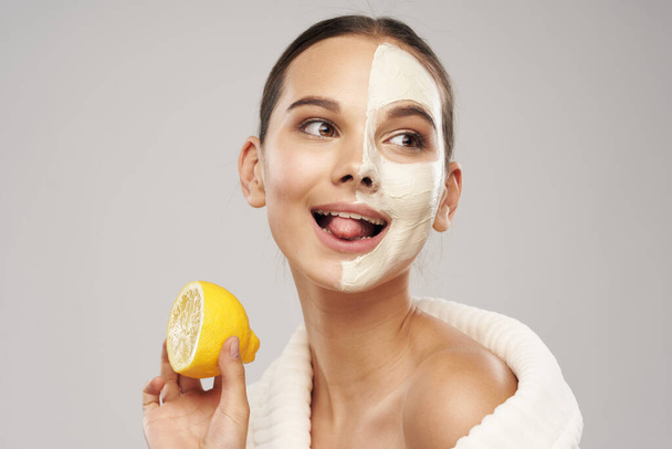 Saubere Haut weiße Maske auf dem Gesicht und ein Stück Zitrone in der Hand Mädchen - Foto, Bild