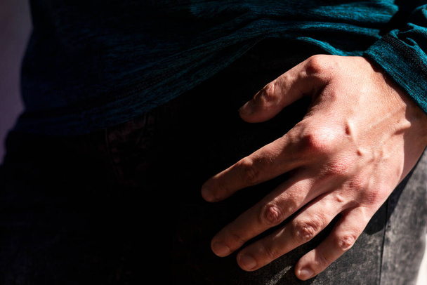 Close up view of Caucasian man's hand under strong natural light with the rest of the body in deep shadow.  - Фото, зображення