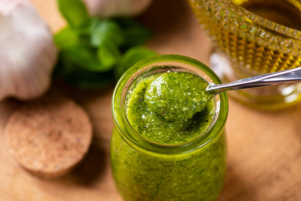 Pesto-Sauce vorhanden. In einem transparenten Glas mit den Zutaten im Hintergrund. Olivenöl, Knoblauch und Basilikum. - Foto, Bild