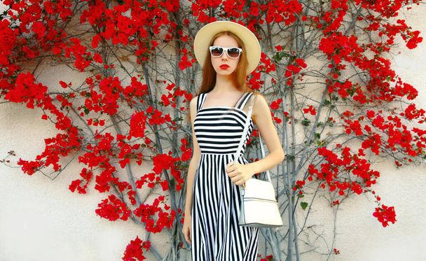 Attractive woman wearing a striped dress and summer straw hat over red flowers background - Photo, Image