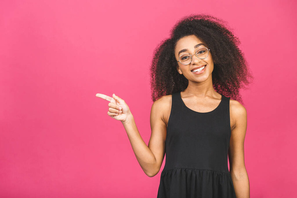 Портрет щасливої молодої афроамериканки, яка спрямовує пальці геть на місце для копіювання ізольовано на рожевому фоні
. - Фото, зображення